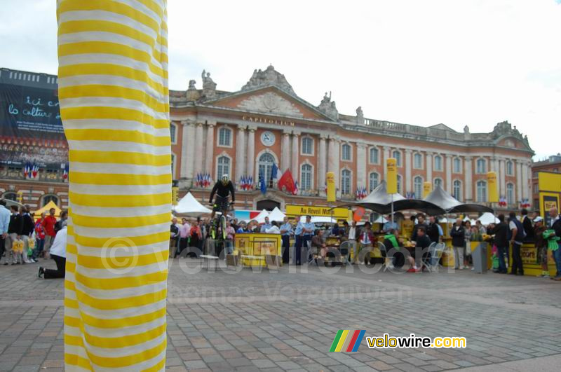 Animation au Village Départ : devant une jambe d'une des femmes en échasses, à l'arrière Marc Vinco sur son VTT Trial